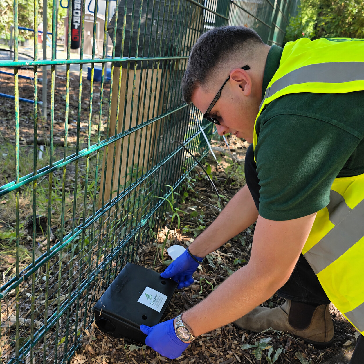 ProLand operative positioning a rodent control station beside a perimeter fence
